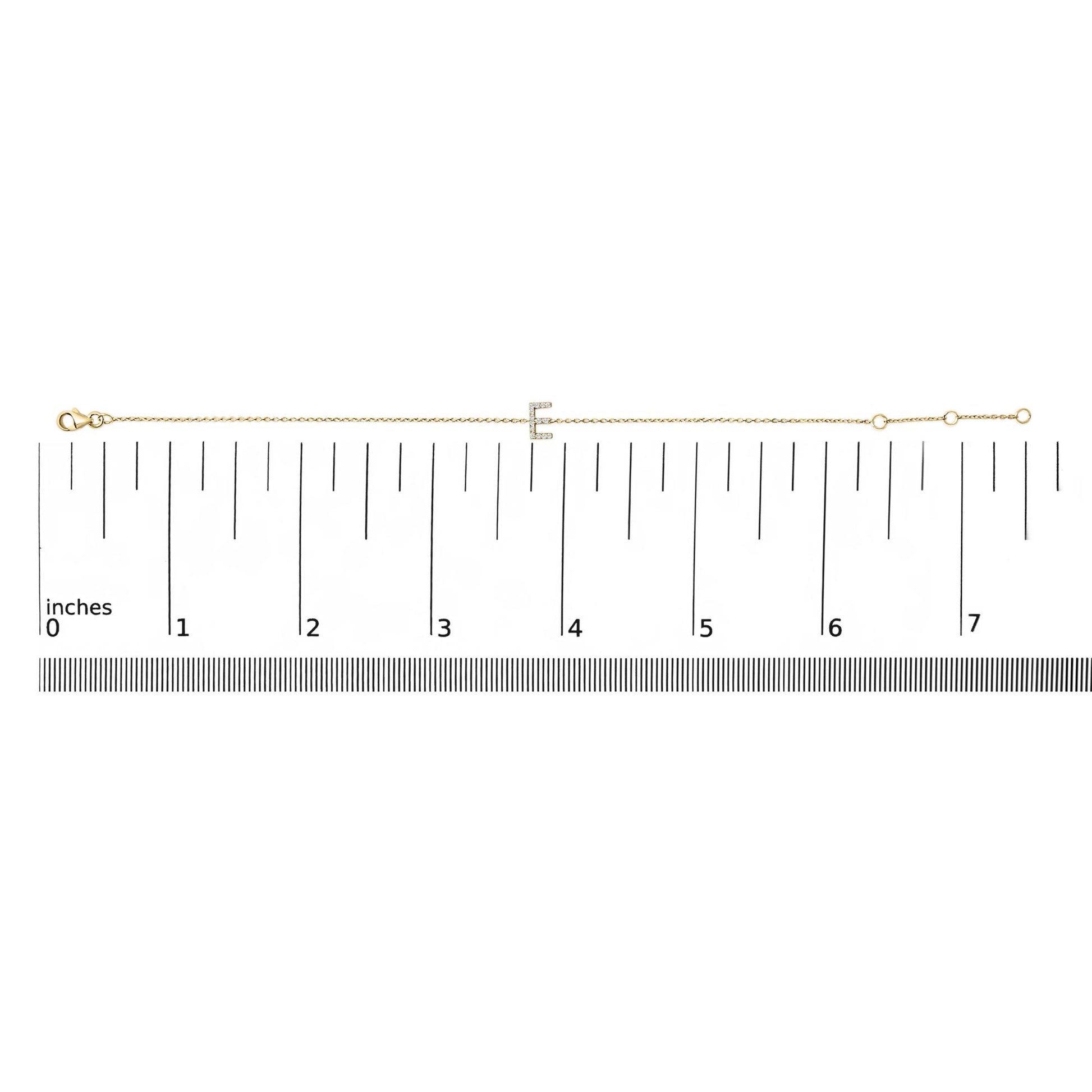 Yellow bracelet with a letter-shaped centerpiece adorned with small white gemstones in micro-pave setting, shown laid flat on a ruler from a top-down angle.
