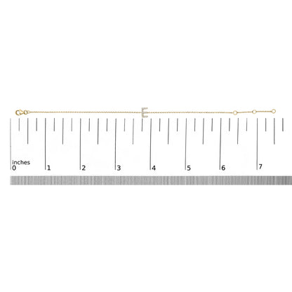 Yellow bracelet with a letter-shaped centerpiece adorned with small white gemstones in micro-pave setting, shown laid flat on a ruler from a top-down angle.