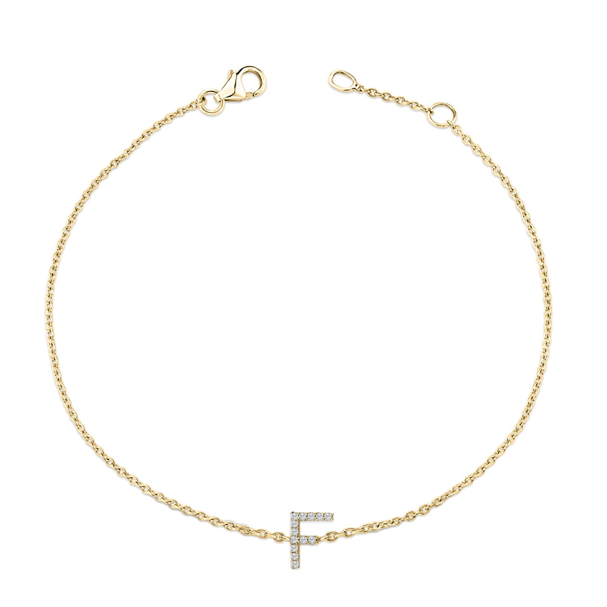 Top-down view of a delicate yellow bracelet with a chain and a letter 'F' charm encrusted with small white gemstones in a micro-pave setting.