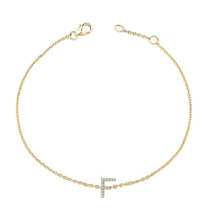 Top-down view of a delicate yellow bracelet with a chain and a letter 'F' charm encrusted with small white gemstones in a micro-pave setting.