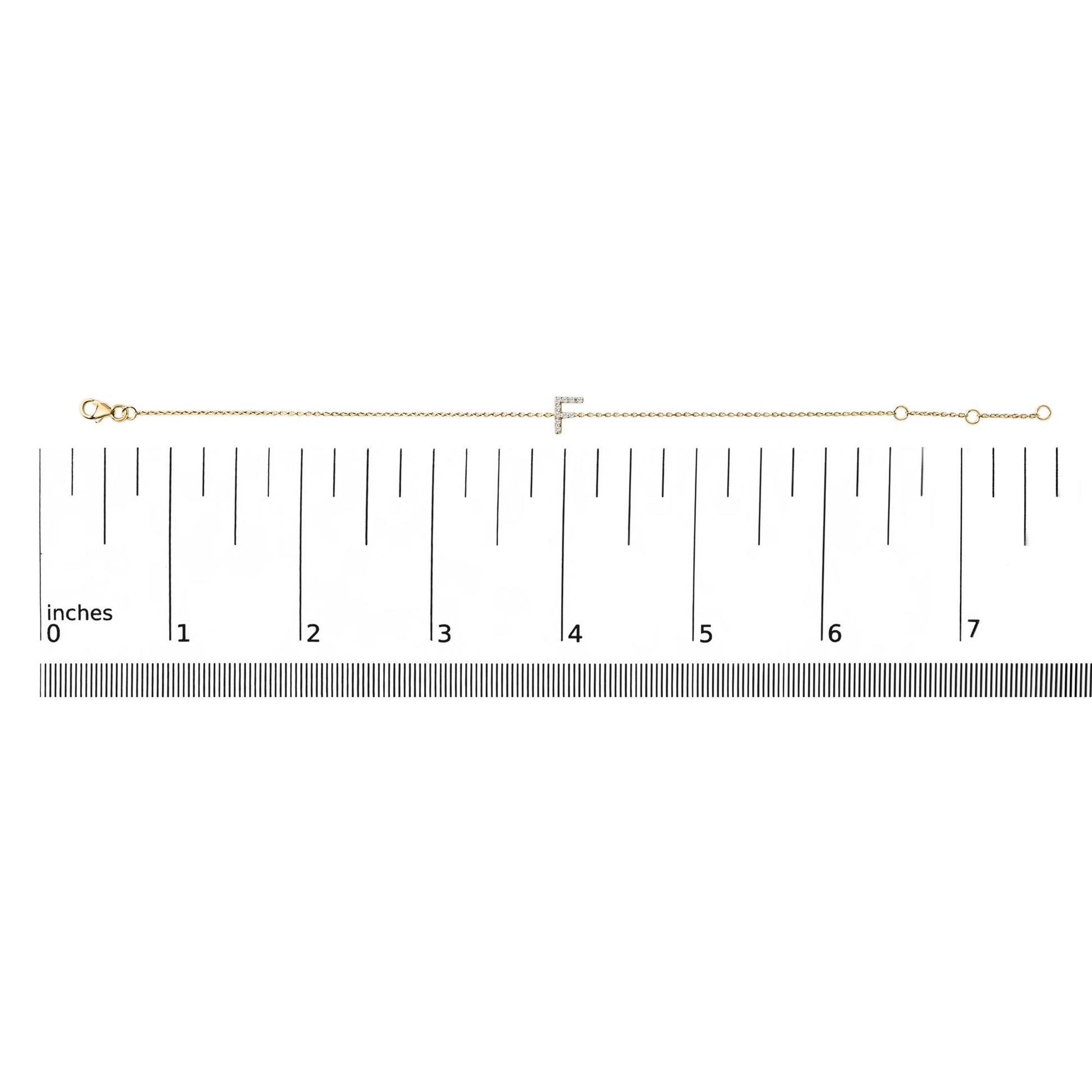 Yellow bracelet with a chain and a horizontal bar encrusted with small white gemstones in micro-pave setting, displayed flat on a measurement scale, top-down view.