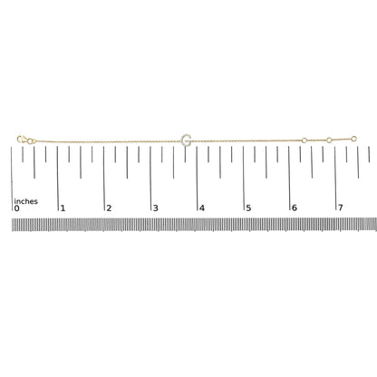 Yellow metal bracelet with a small circular charm encrusted with white gemstones, shown flat on a ruler scale in a top-down angle.