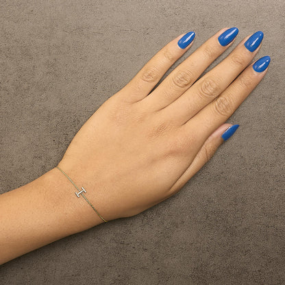 Yellow metal bracelet with a horizontal bar featuring white gemstones in micro-pave setting, shown on a model's wrist from a top-down angle.