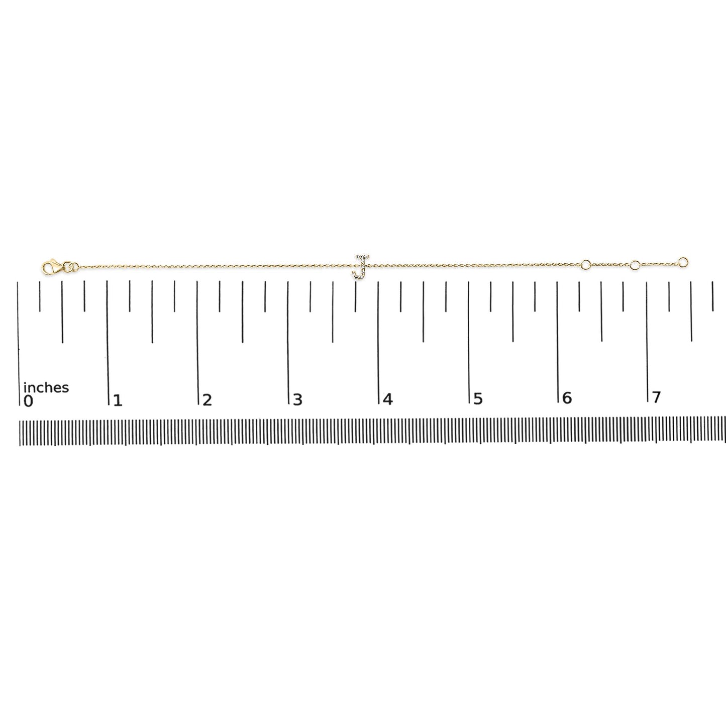 Yellow metal bracelet with a small 'J' charm set with white gemstones, shown lying flat on a measuring scale, top-down angle.