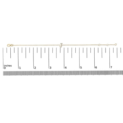 Yellow metal bracelet with a small 'J' charm set with white gemstones, shown lying flat on a measuring scale, top-down angle.