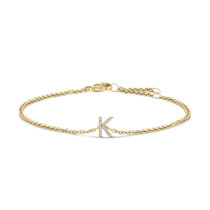 Yellow metal bracelet with a chain design and a letter 'K' centerpiece adorned with white gemstones, shown from a top-down angle on a white background.