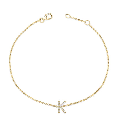 Yellow metal bracelet with a chain and a letter 'K' charm adorned with small white gemstones in a micro-pave setting, shown from a top-down angle on a white background.
