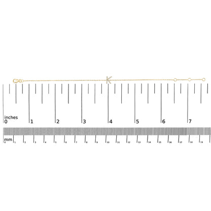 Yellow bracelet with a chain design featuring a letter adorned with small white gemstones, shown on a scale from a top-down angle.