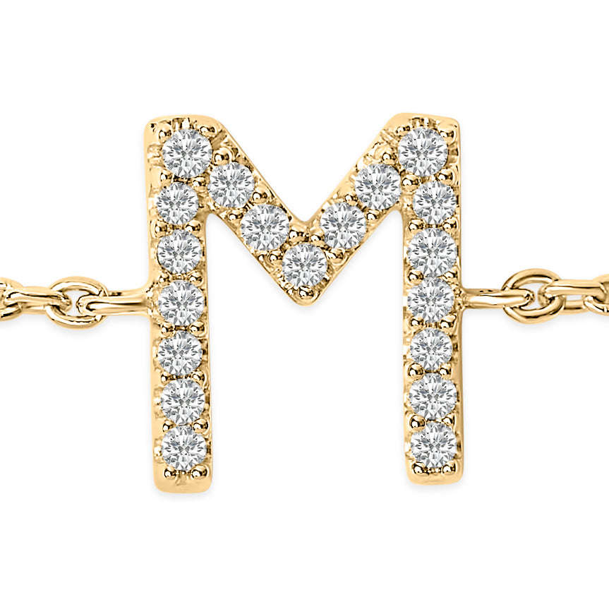 Close-up front view of a yellow metal bracelet featuring an 'M' shaped charm adorned with round white gemstones in a micro-pave setting.