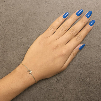 Yellow metal bracelet with a zigzag design adorned with white round gemstones in a micro-pave setting, shown on a model's wrist from a top-down angle.