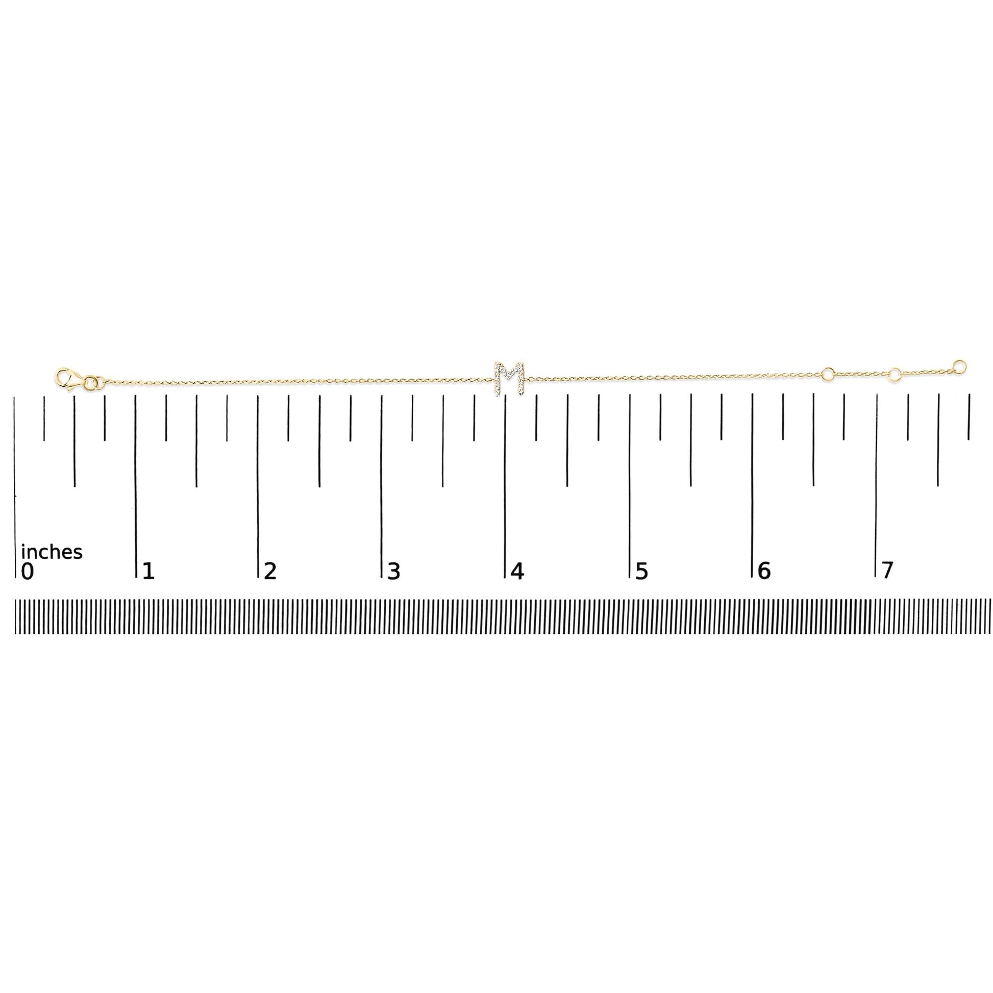 Thin yellow bracelet with a central letter 'M' embellished with small white gemstones in a micro-pave setting, shown laid flat on a scale from above.