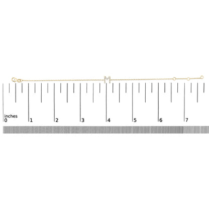 Thin yellow bracelet with a central letter 'M' embellished with small white gemstones in a micro-pave setting, shown laid flat on a scale from above.