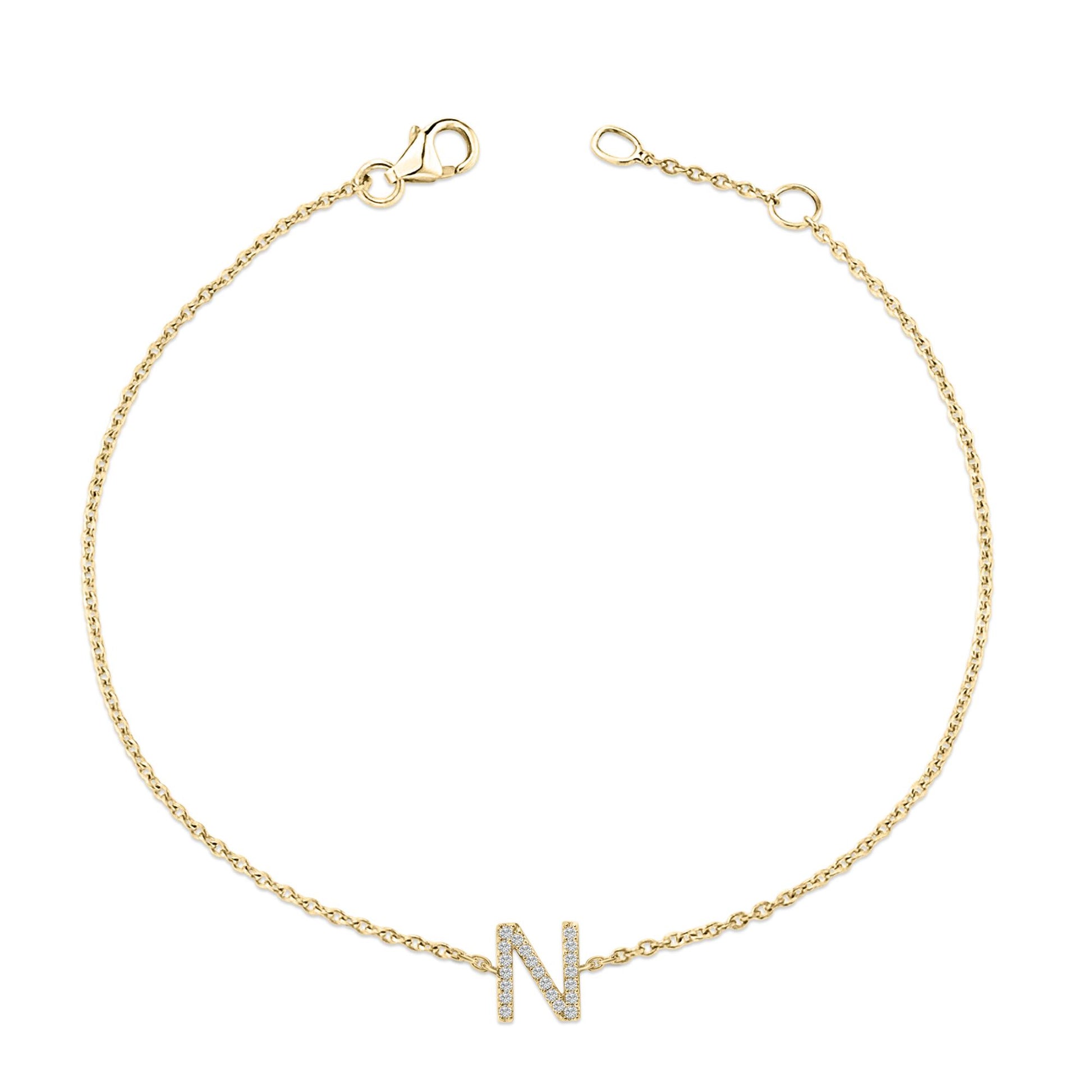 Yellow metal bracelet with a chain and a central letter 'N' adorned with small white gemstones in a micro-pave setting, shown from a top flat lay angle.