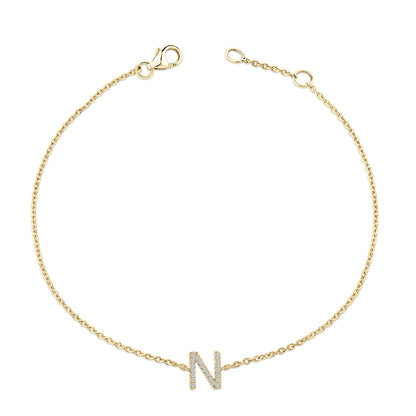 Yellow metal bracelet with a chain and a central letter 'N' adorned with small white gemstones in a micro-pave setting, shown from a top flat lay angle.