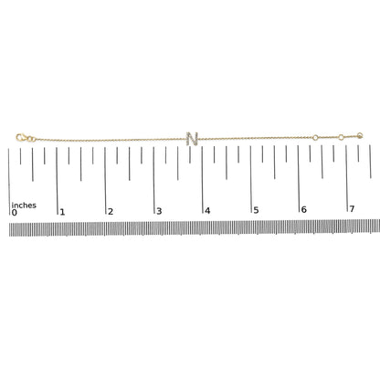 Thin yellow bracelet with a central letter 'N' adorned with small white gemstones in a micro-pave setting, shown on a scale from a top-down angle.