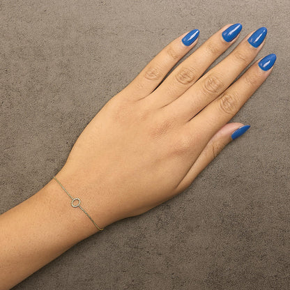 Yellow metal delicate bracelet with a small circular centerpiece set with white gemstones in a micro-pave setting, shown worn on a model's wrist, top-down angle.