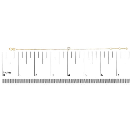 Yellow metal bracelet with a micro-pave set white gemstone initial charm, shown on a ruler scale from a top-down angle.