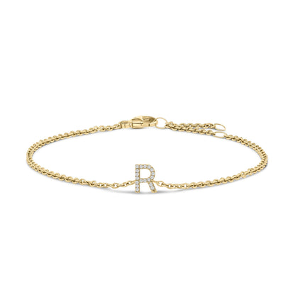 Close-up front angle of a yellow metal bracelet with a chain and a central letter 'R' adorned with small white gemstones in a micro-pave setting, shown on a white background.