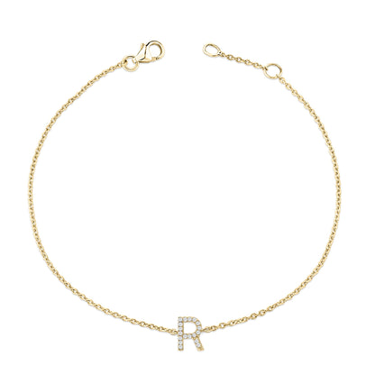 Yellow metal bracelet with a chain design and a central letter 'R' embellished with small white gemstones, shown from a top-down angle on a white background.