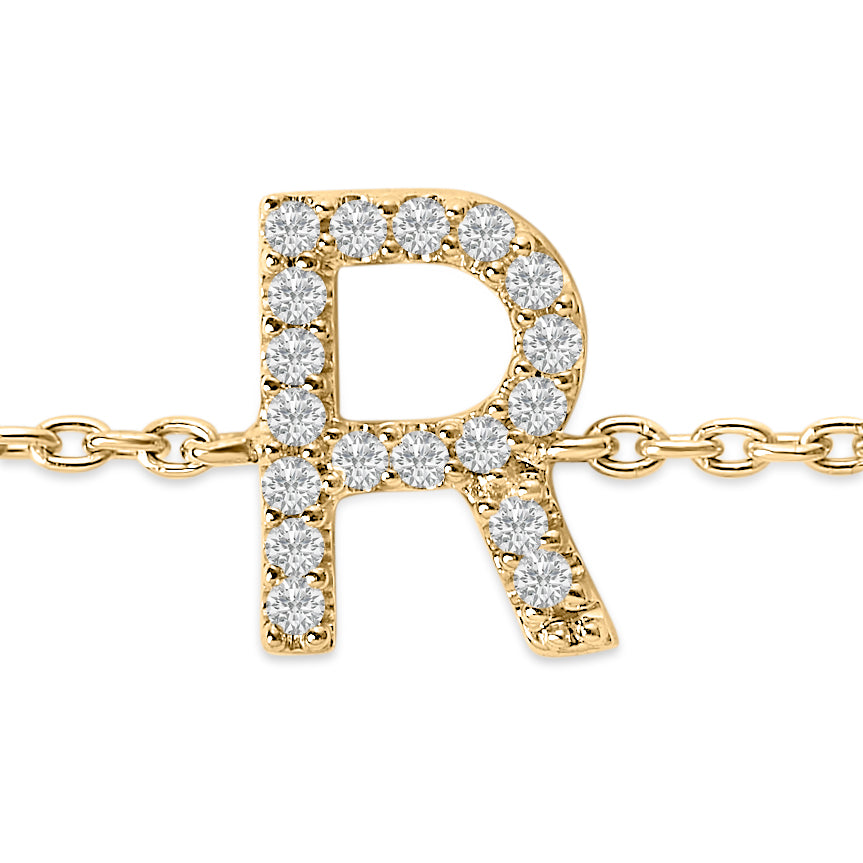 Close-up front view of a yellow metal bracelet featuring a capital letter 'R' pendant adorned with round white gemstones in a micro-pave setting on a linked chain.