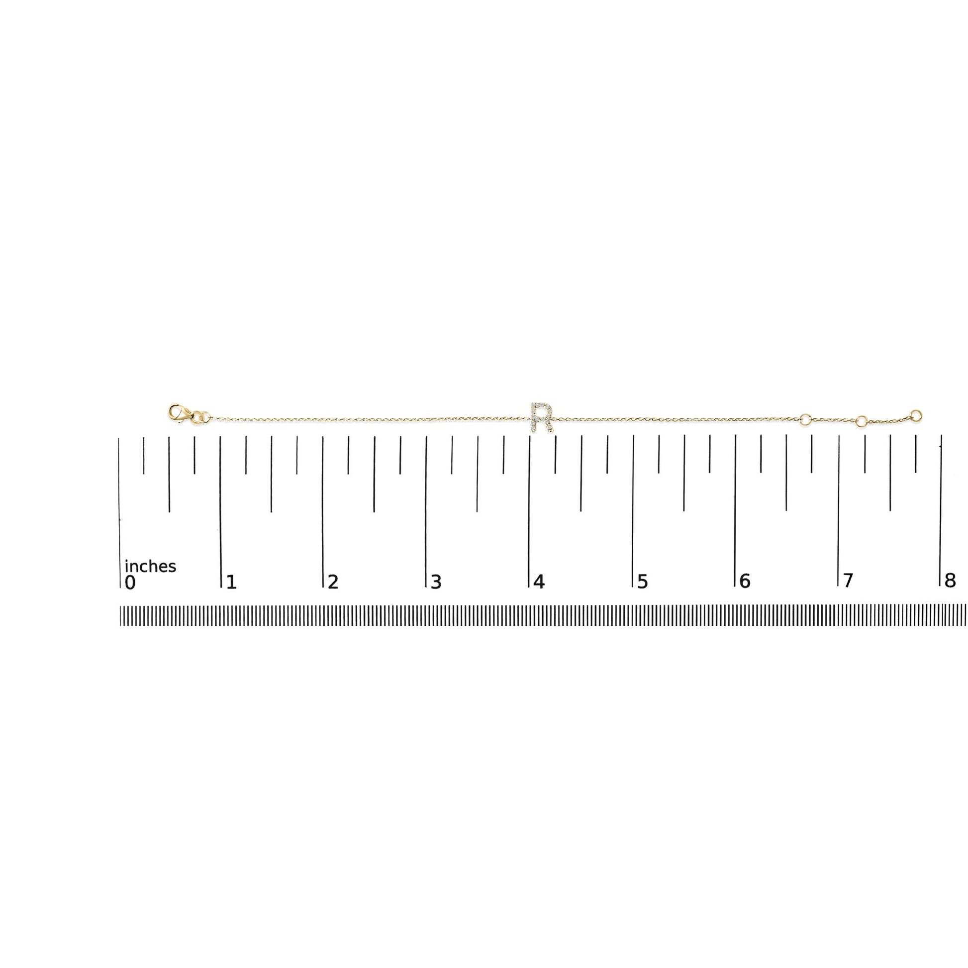 Yellow bracelet with a central letter 'R' set with small white gemstones in a micro-pave setting, displayed flat on a measurement scale, top-down angle.