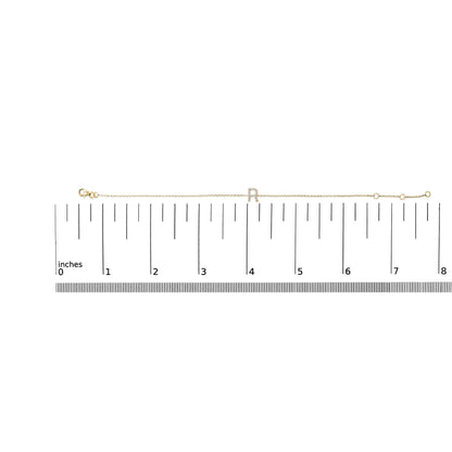 Yellow bracelet with a central letter 'R' set with small white gemstones in a micro-pave setting, displayed flat on a measurement scale, top-down angle.