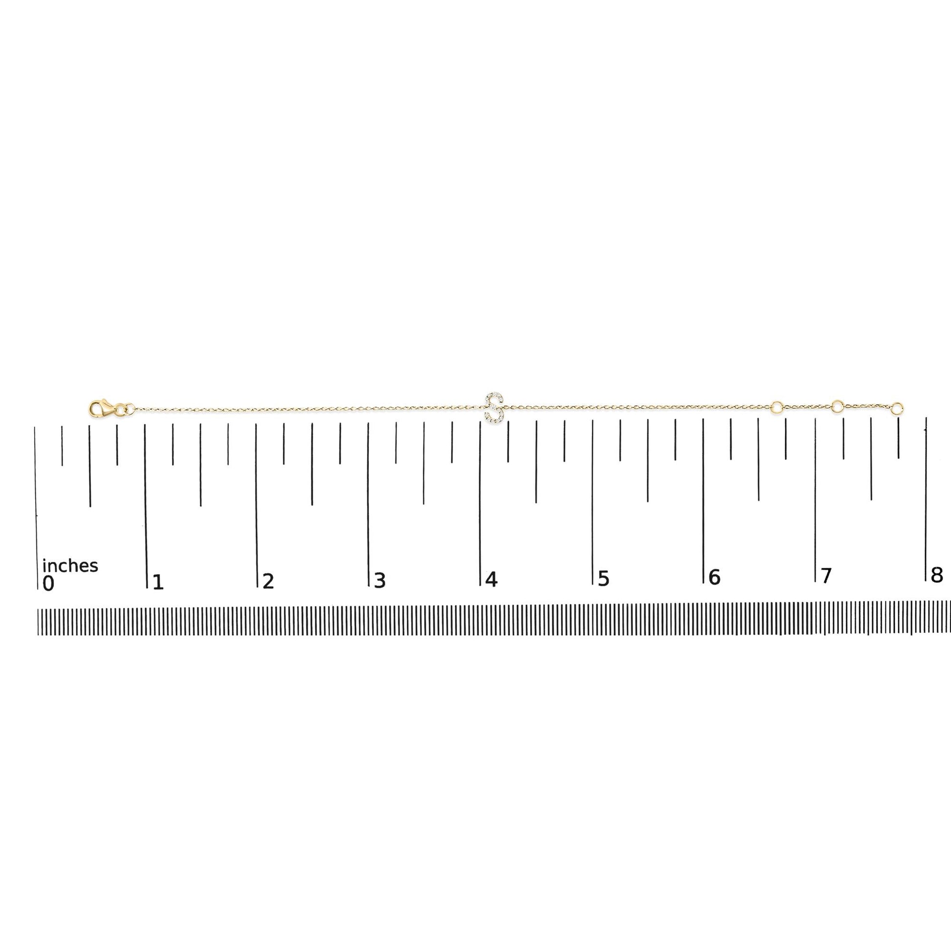 Thin yellow bracelet with a small curved centerpiece set with white round gemstones in a micro-pave style, shown flat on a ruler from a top-down angle.