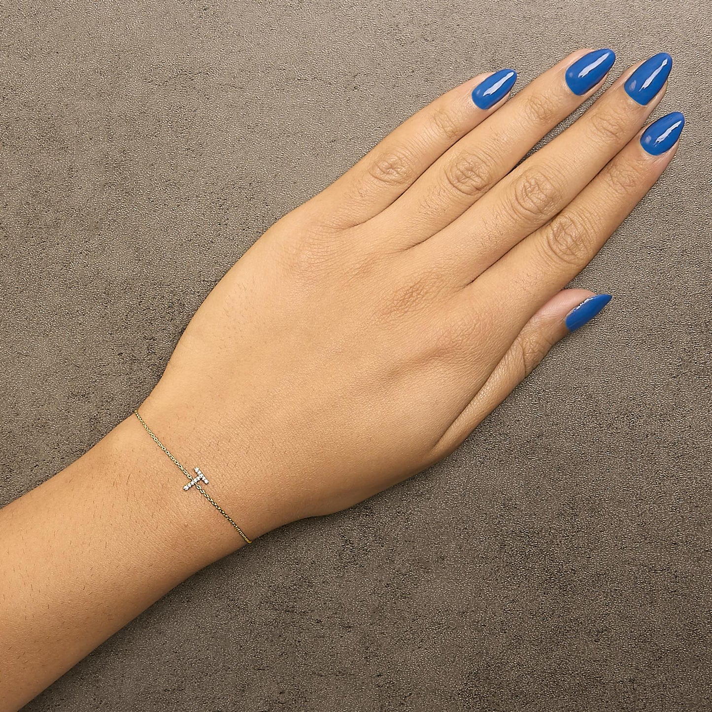 Yellow metal delicate bracelet with a horizontal T-shaped charm featuring white round micro-pave gemstones, shown worn on a model's wrist from above.