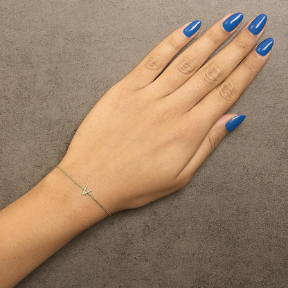 Bracelet shown worn on a model's wrist, viewed from above, featuring a delicate yellow chain with a small V-shaped accent studded with white gemstones in a micro-pave setting.