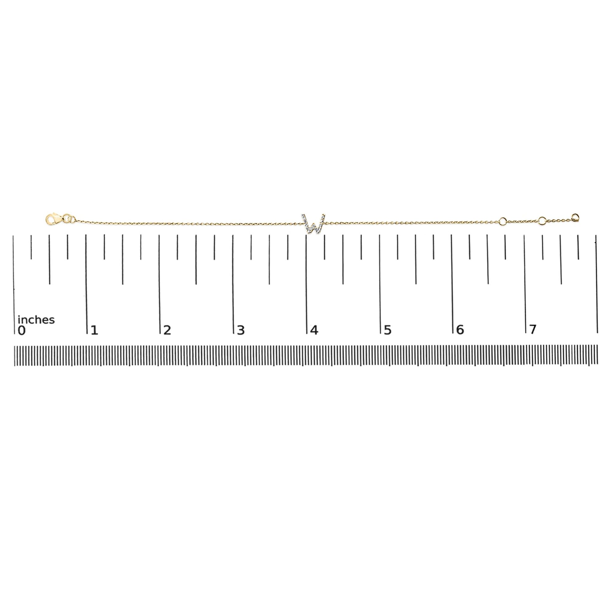 Yellow metal bracelet with a central 'W' initial accented by white gemstones in a micro-pave setting, shown laid flat on a ruler scale from a top-down angle.