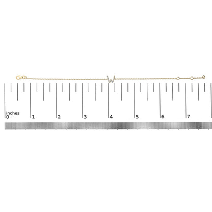 Yellow metal bracelet with a central 'W' initial accented by white gemstones in a micro-pave setting, shown laid flat on a ruler scale from a top-down angle.