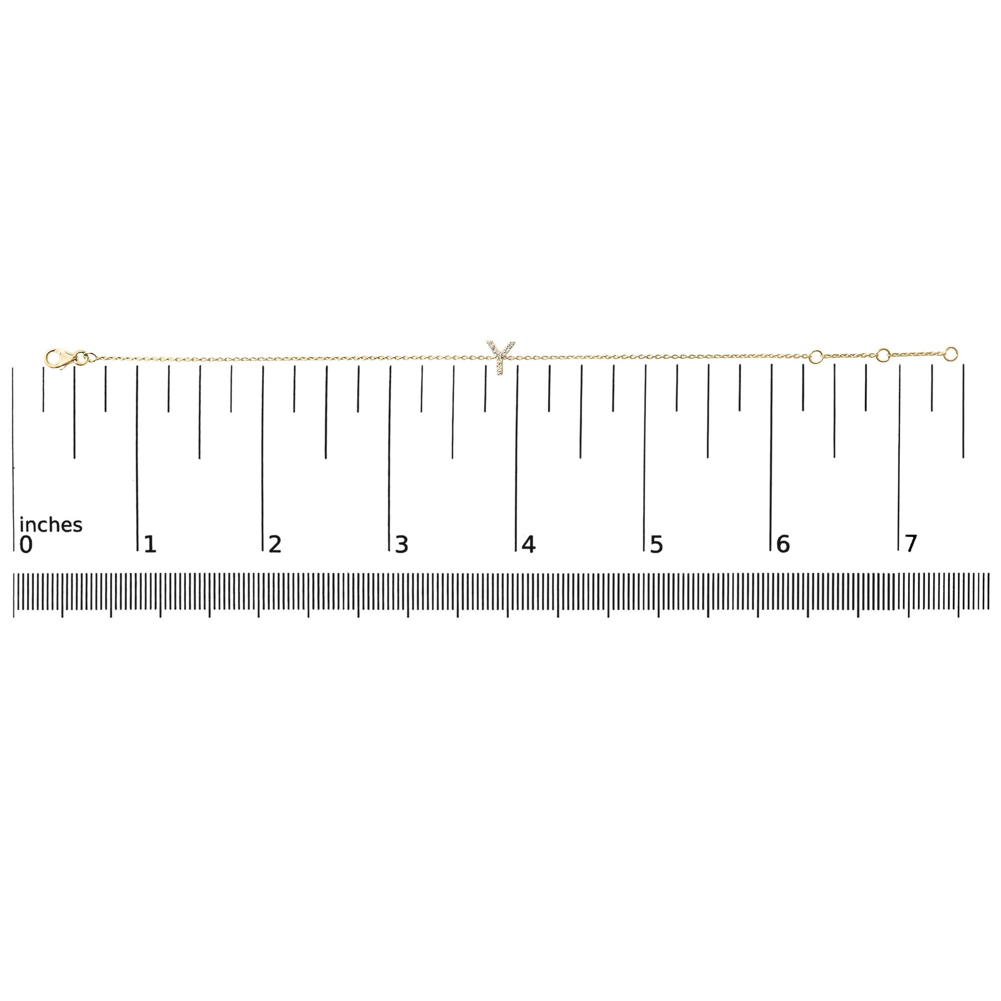 Yellow metal bracelet with a delicate chain and a small 'Y' shaped charm featuring white gemstones, shown flat on a ruler measuring approximately 7 inches, top-down angle.