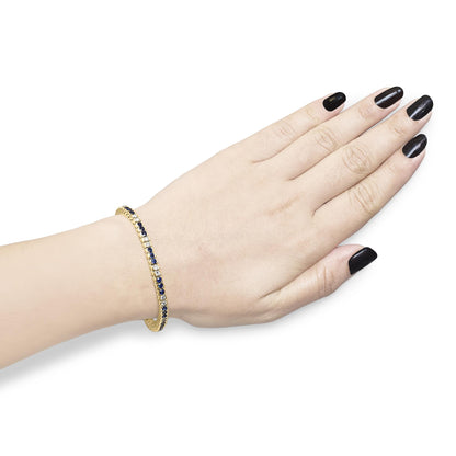 Yellow metal bracelet with alternating white and blue round gemstones in bezel settings, shown on a model's wrist from a top angle.