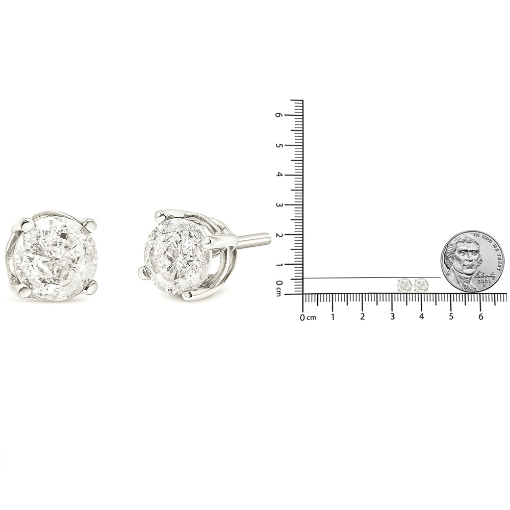 Pair of white metal stud earrings with round white gemstones in four-prong settings, shown from front and side angles, next to a ruler and a coin for size reference.