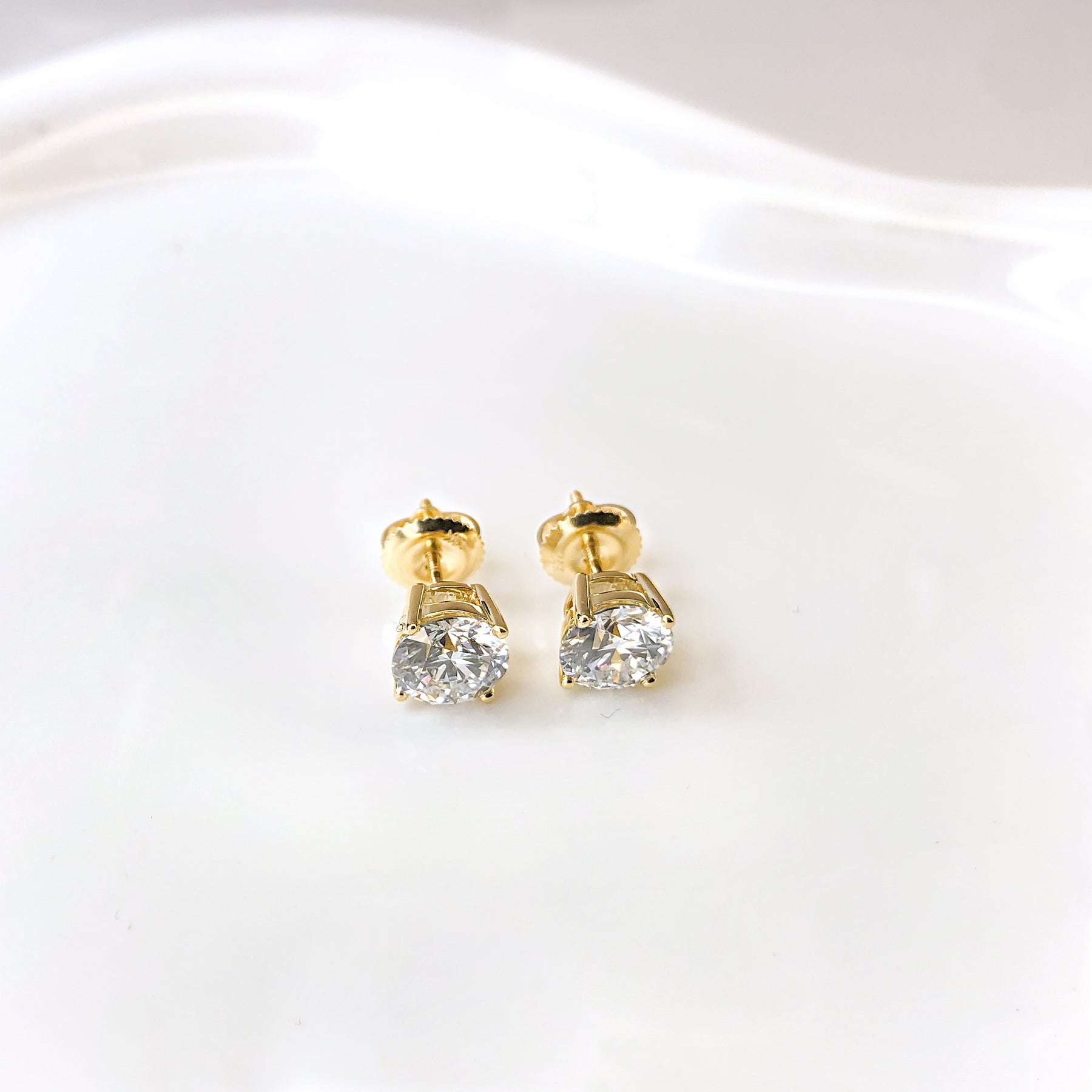 Haus of Brilliance gold diamond stud earrings laying flat on a surface
