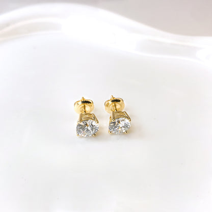 Pair of yellow metal stud earrings with round white gemstones in 4-prong settings, shown from front angle on a white surface.