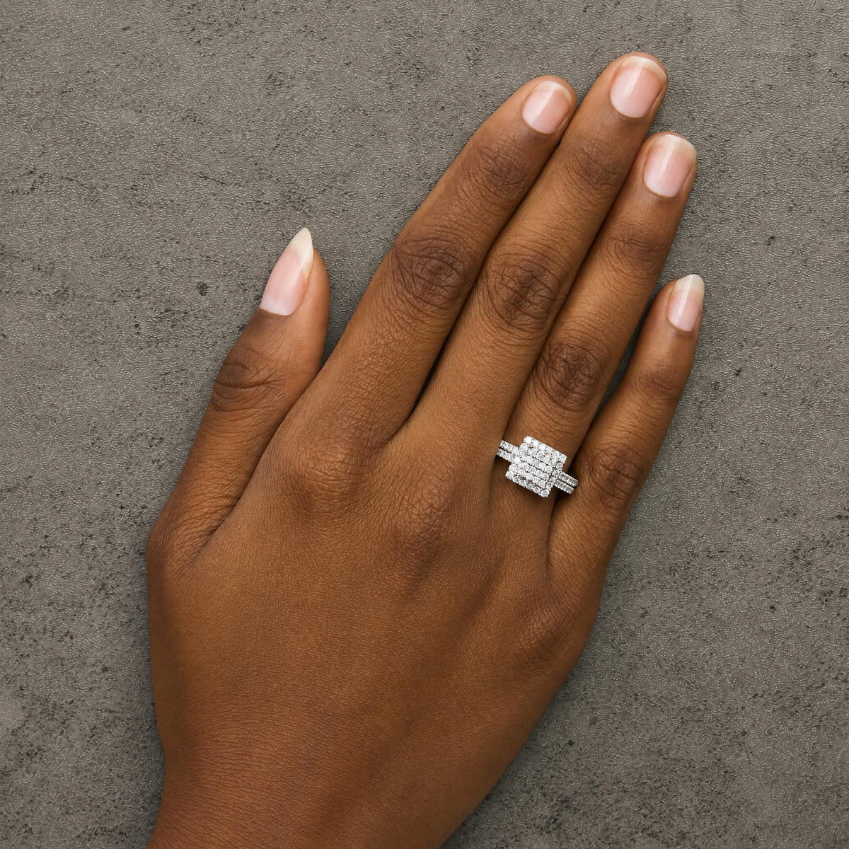 Close-up front angle of a model's hand wearing a white metal ring featuring multiple rows of round white gemstones in prong settings, forming an intricate square design at the center.
