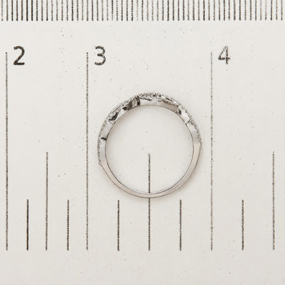 White ring with small round white gemstones in prong setting encircling the band, shown flat on a ruler for scale, viewed from above.