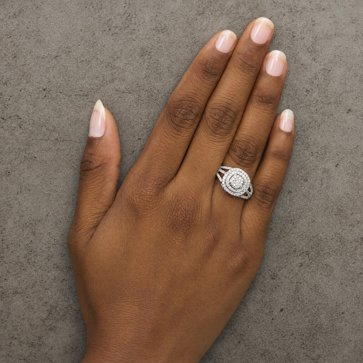 Close-up angle of a model's hand wearing a white ring with multiple round white gemstones in prong settings arranged in concentric circular patterns.