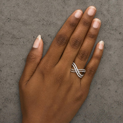 Close-up top view of a model's hand wearing a white ring with round white gemstones set in prongs, featuring an overlapping design.