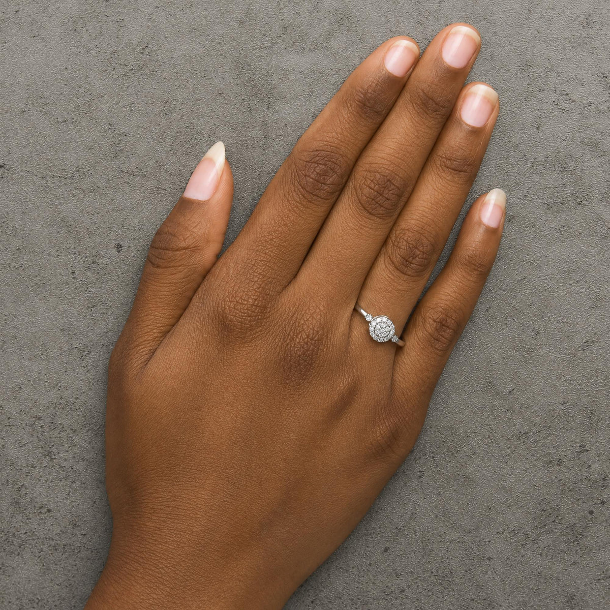 White metal ring with round white gemstones in prong settings forming a cluster, shown worn on a model's hand from a top-down angle.