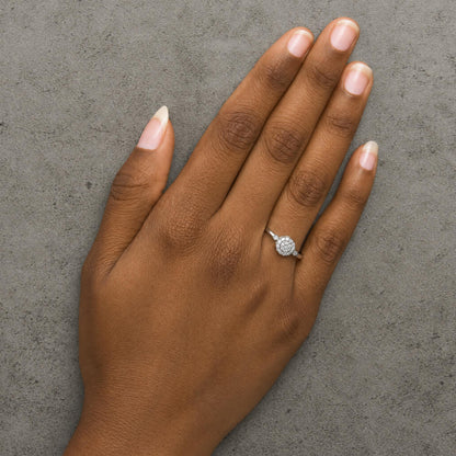 White metal ring with round white gemstones in prong settings forming a cluster, shown worn on a model's hand from a top-down angle.