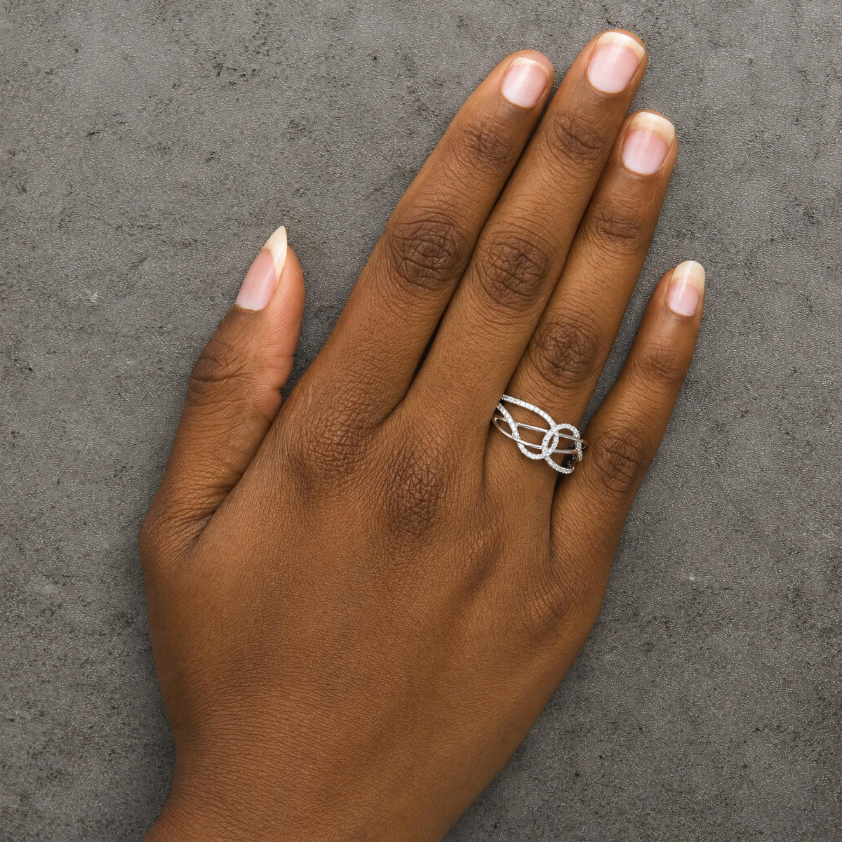 Close-up front angle of a model's hand wearing a white metal ring featuring multiple loops encrusted with round white gemstones in prong settings.