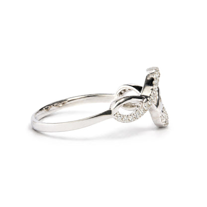 Close-up angled side view of a white ring featuring an intricate design with multiple loops adorned with small round white gemstones in prong settings.