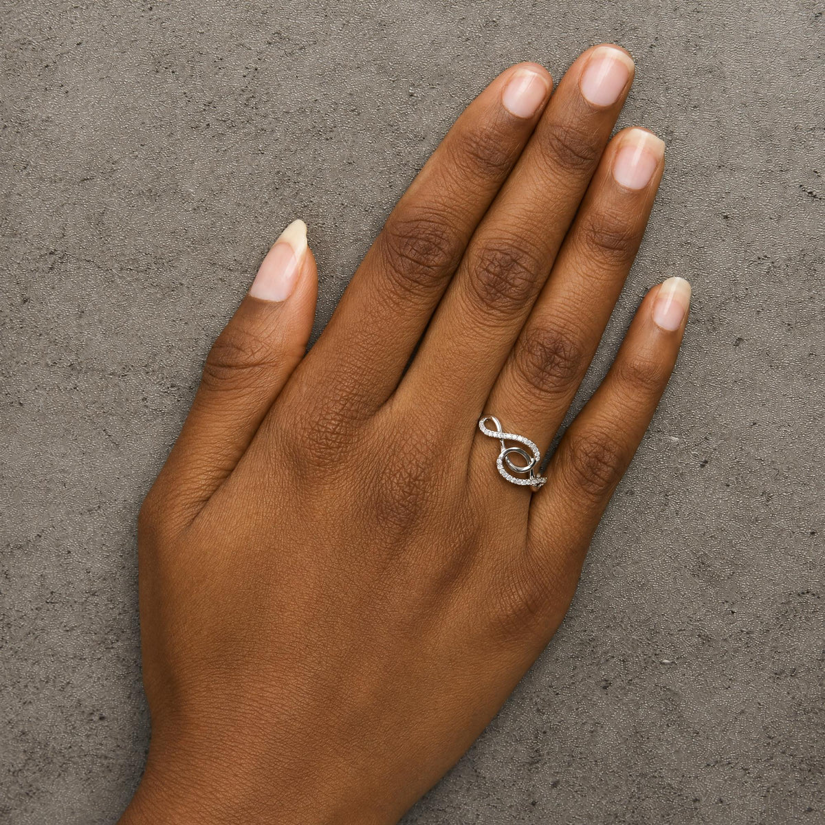 White metal ring with an abstract swirl design and small round white gemstones in prong settings, shown worn on a model's finger, angled top down.