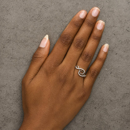 White metal ring with an abstract swirl design and small round white gemstones in prong settings, shown worn on a model's finger, angled top down.