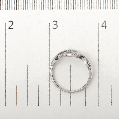 Close-up image of a white metal ring with two intertwined bands, each set with round white gemstones in prong settings, shown on a measurement scale.