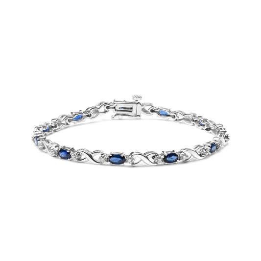White metal bracelet with alternating oval blue gemstones and round white gemstones in prong settings, shot from a slightly elevated front angle.