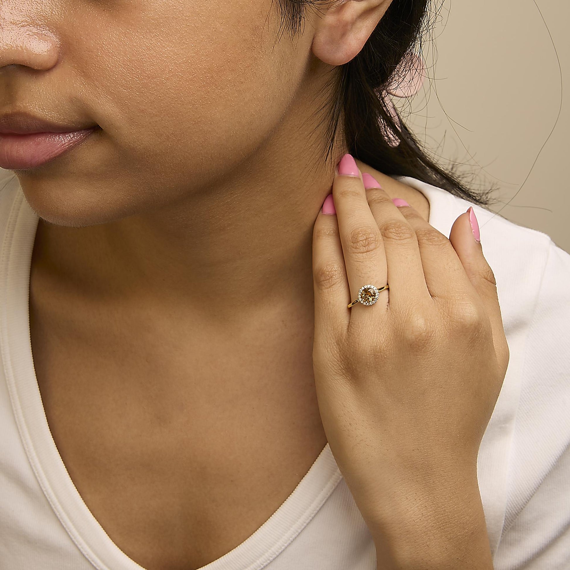 Yellow metal earrings with round orange gemstones surrounded by round white gemstones, shown worn on a model from a side angle.