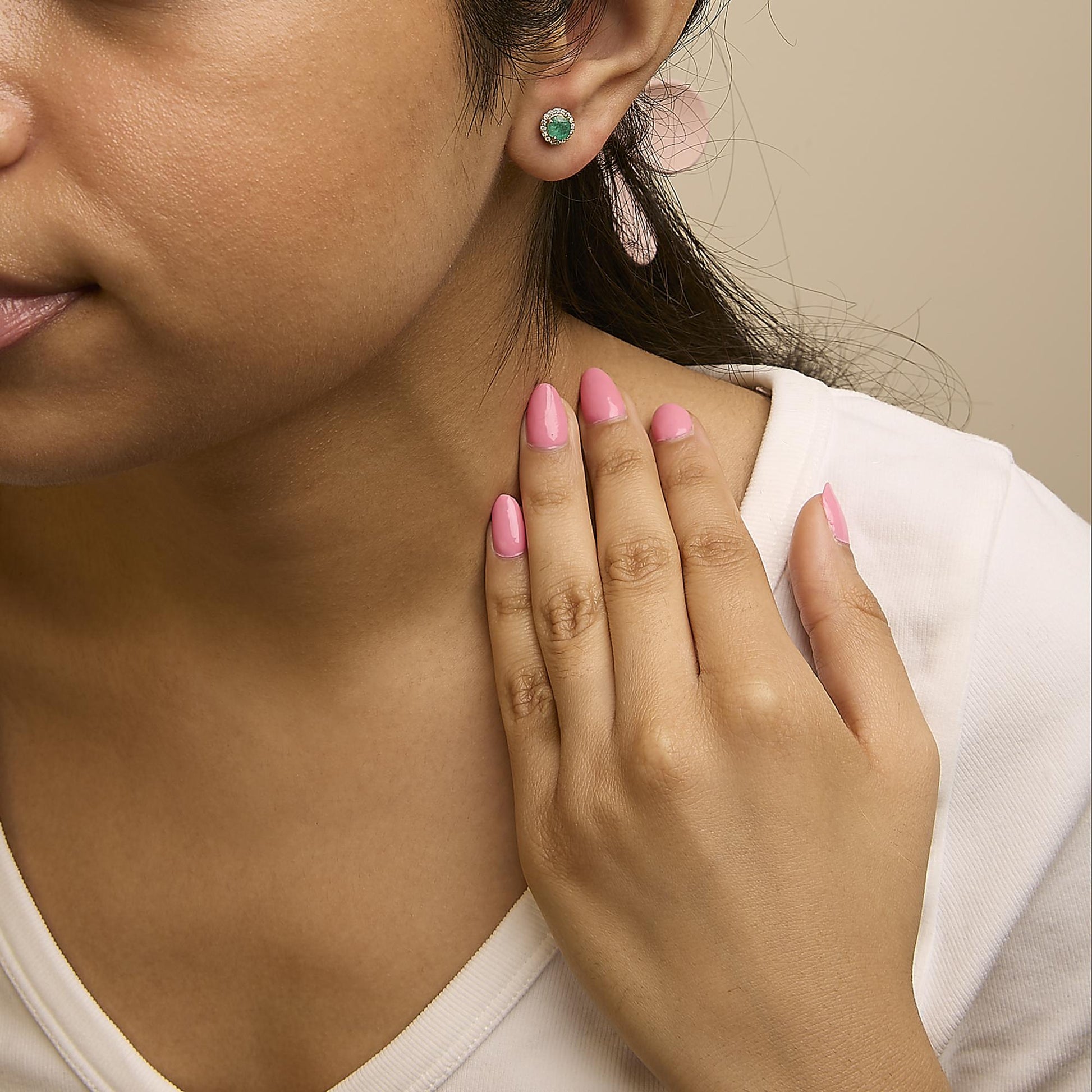 Close-up front angle of a model wearing round yellow metal stud earrings featuring a green round gemstone center surrounded by small white round gemstones in a shared prong setting.